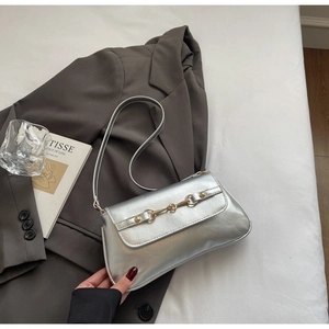 Détail du sac baguette argenté vintage avec mors doré sur fond de blazer gris élégant