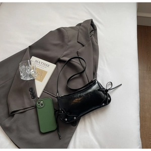 Flachbild einer schwarzen glänzenden Sichel-Tasche mit Nieten und Schleifendetails