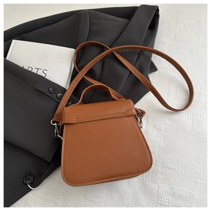 Brown leather bucket bag with top handle and strap shown on a flat surface