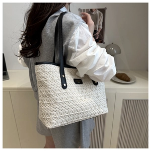 Close-up of beige woven tote bag with black trim and brand logo on shoulder