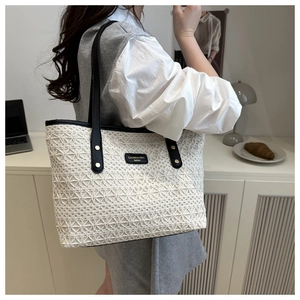 Detail of white woven tote bag with black leather straps and brand label in use