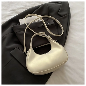 Dettaglio di una borsa a mezzaluna color crema minimalista su un blazer con texture