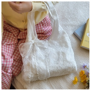 Detail view of a white lace tote bag featuring a large bow and floral crochet patterns