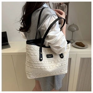 Close-up of white woven lace tote bag featuring black leather handles and logo patch