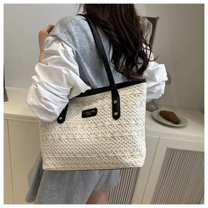 Detail of hollow-out woven tote with black leather straps and gold metal rivets