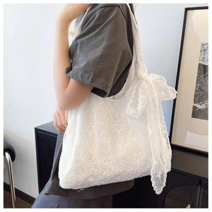 Detail of white lace tote bag with floral embroidery and large decorative bow accessory