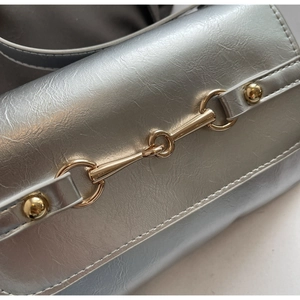 Détail macro du sac argenté avec boucle mors de cheval dorée et coutures de précision