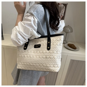 Close-up of crochet tote bag with black trim and brand logo plate worn by a model