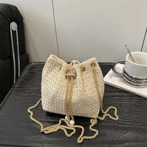 Minimalist woven bucket bag with gold chain strap and pearl accents on a dark surface