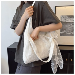 Close-up of white lace embroidery shoulder bag with floral patterns and a side bow detail