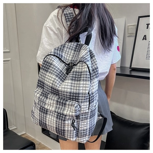 Detailed view of the gray checkered backpack being worn by a model in a modern room