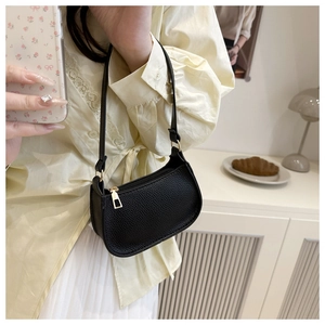 Close-up of black lychee grain leather underarm bag with gold hardware on a woman shoulder