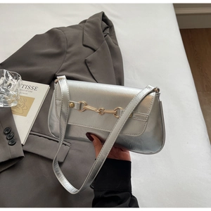 Détail du sac argenté avec boucle mors dorée vintage sur fond de costume gris élégant