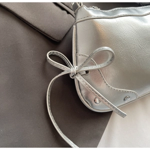 Detail der silbernen Metallic-Sichelbag mit Schleifenkontur und Nietenverzierung