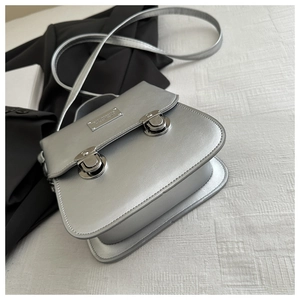 Detail of silver metallic crossbody satchel with dual buckles and polished finish