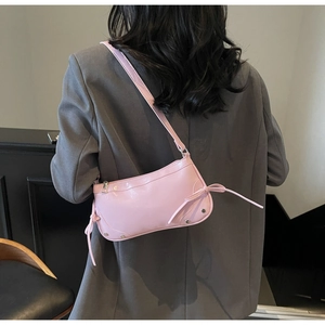 Nahaufnahme einer rosa glänzenden Y2K-Halbmondtasche mit silbernen Nieten und Bändern