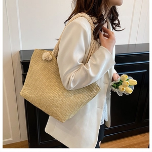 Detail of hand-woven straw tote bag with decorative knot handles on a female model