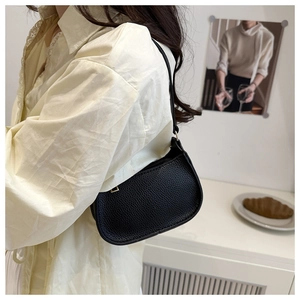 Detail of black pebbled leather texture on minimalist shoulder bag worn by model