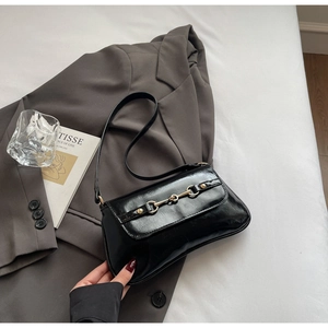 Détail du sac baguette noir brillant avec boucle mors dorée et bandoulière élégante