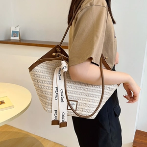 Women's woven tote bag with brown leather trim and stylish webbing straps in a minimalist room