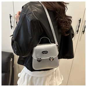 Detail of silver metallic crossbody bag with double buckles worn by a model