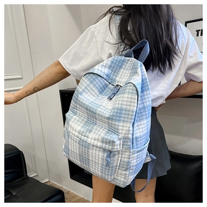 Blue and white checkered canvas backpack worn by model in a casual indoor setting