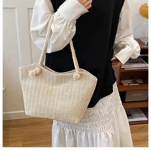 Close-up of beige straw tote bag with braided hemp handles and two decorative pompoms