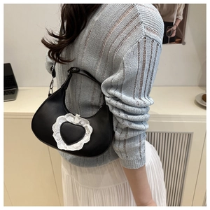 Detail of black crescent bag featuring a white lace heart patch and matte PU leather texture