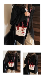 Detail of cherry print tote bag with red handles and matching cherry charm accessory