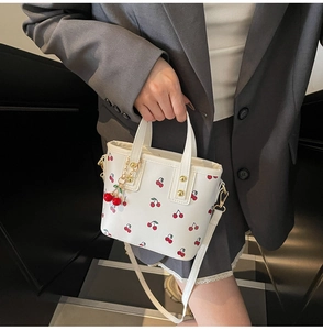 Detailed view of a white cherry print bucket bag with golden hardware and charm on a model