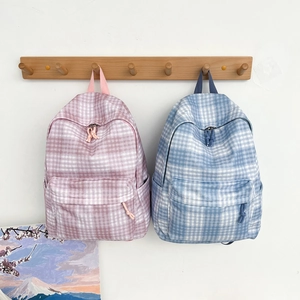 Detail view of pink and blue checkered canvas backpacks hanging on wooden wall hooks