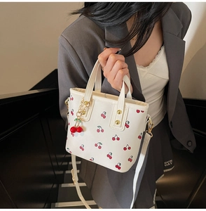 Détail du cabas blanc à motif cerise avec charm 3D rouge et bandoulière réglable