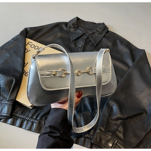 Détail du sac à bandoulière argenté avec boucle mors dorée sur fond de veste en cuir