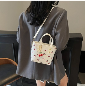 Detail view of white cherry print bucket bag showing red cherry charms and shoulder strap