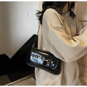 Détail du sac porté épaule noir brillant avec boucle dorée et fine bandoulière en cuir