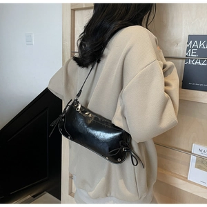 Detail einer schwarzen glänzenden Lackleder-Schultertasche mit dekorativer Seitenschleife