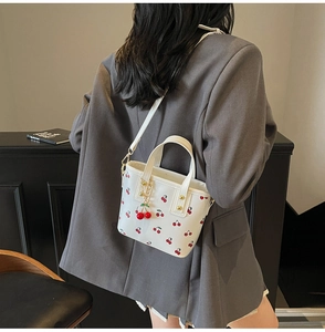 Detail of white cherry print bucket bag with metal strap and cute cherry pendant accessory