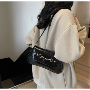 Détail du sac sous l'aisselle en cuir verni noir avec boucle mors dorée chic