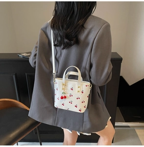 Detail of white cherry print tote bag with 3D cherry charm and metal chain accessory