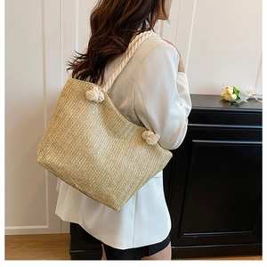 Detail of hand-woven straw tote bag with chunky white rope handles and decorative pom-poms