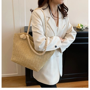 Detail of straw woven tote bag featuring soft cream rope straps and decorative pom-poms