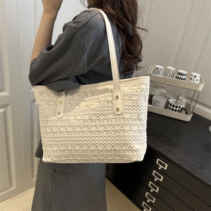 White woven straw tote bag with leather strap and metal logo plate shown in lifestyle setting