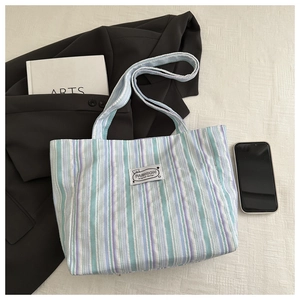 Detail of blue and purple striped canvas tote bag with fashion label and long strap