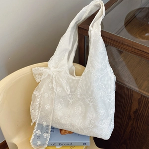 French vintage white lace floral tote bag with a large bow on a cream chair