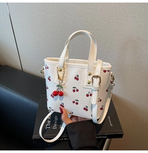 Close-up of white cherry print bucket bag with golden hardware on a black book