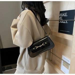 Détail du sac à bandoulière en cuir verni noir avec boucle mors dorée sur un mannequin