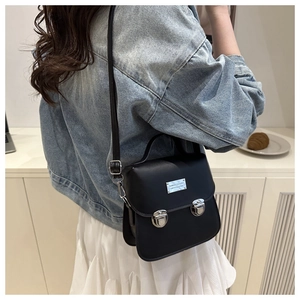 Detail of a black crossbody bag with silver buckles shown in a casual lifestyle setting