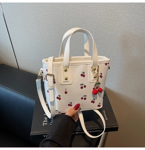Detail of white cherry print handbag featuring red cherry charm and adjustable strap