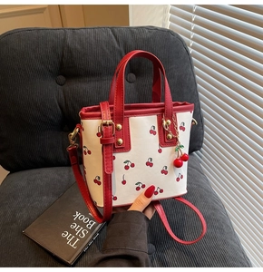 Detail of white tote bag with red cherry print featuring metal cherry charm and red straps