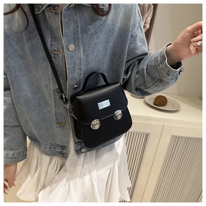 Detail of a black mini crossbody bag with silver hardware on a casual outfit